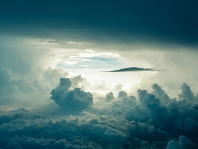 Blick von zwischen zwei Wolkenschichten einem Loch zum blauen Himmel entgegen